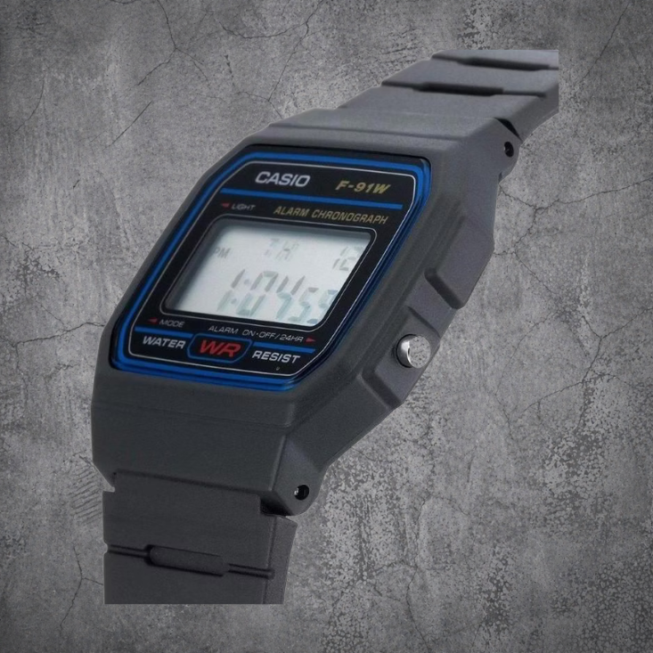 `Schwarze CASIO F-91W-1YEG Digitaluhr mit Resin-Armband in Seitenansicht auf grauem Betonhintergrund`
