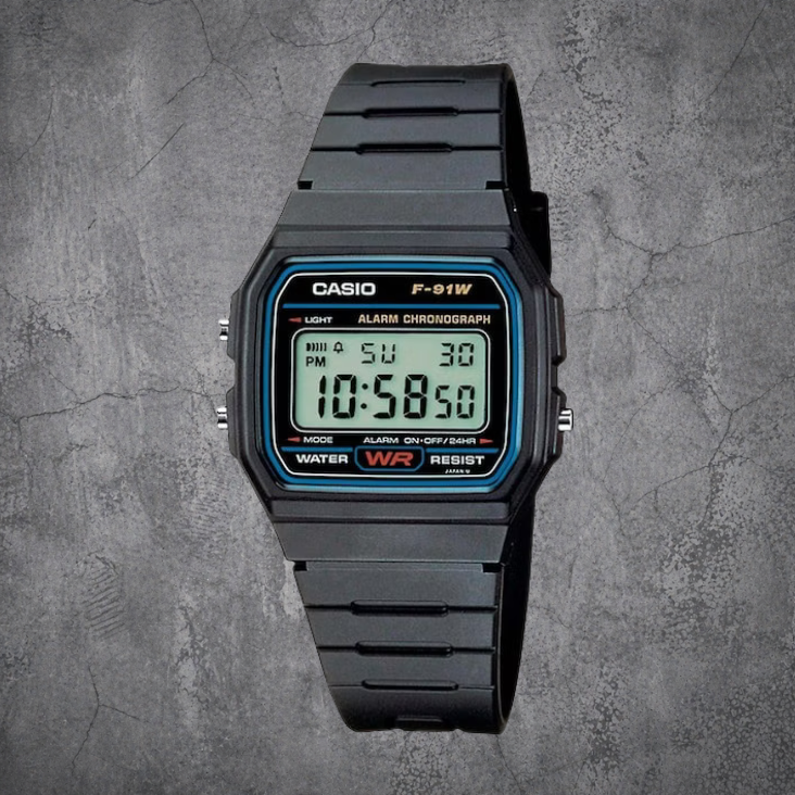 Schwarze CASIO F-91W-1YEG Digitaluhr mit Resin-Armband in Frontansicht auf grauem Betonhintergrund