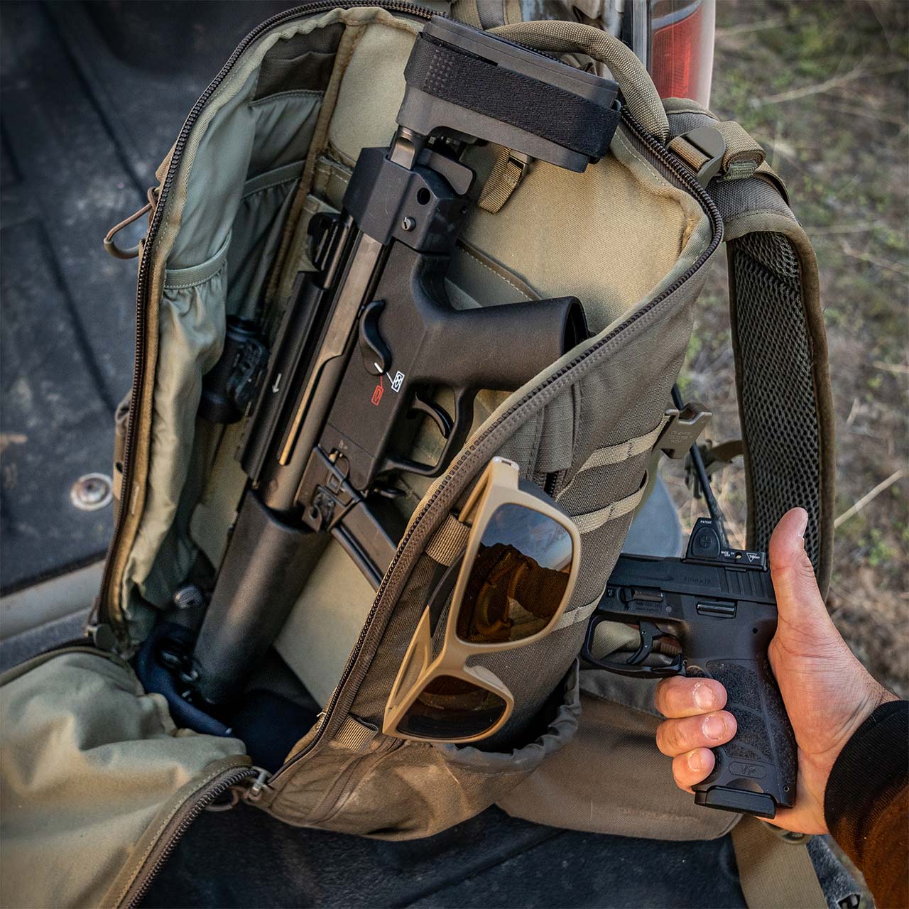 `Geöffneter Tactical Rucksack mit Outdoor-Ausrüstung und Schutzbrille im Einsatzstil bei natürlicher Umgebung`
