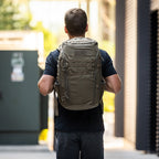 `Person mit olivgrünem Tactical Rucksack im Urban Outdoor-Stil bei Tageslicht`
